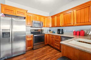 Kitchen with appliances with stainless steel finishes, dark wood finished floors, brown cabinetry, a textured ceiling, and a sink
