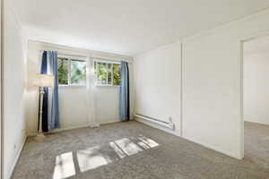 Carpeted spare room featuring a baseboard radiator