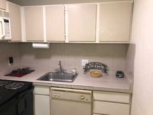 Kitchen with white appliances, a sink, backsplash, and white cabinetry