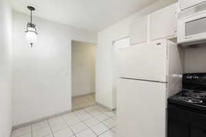 Kitchen with white appliances, white cabinets, baseboards, decorative light fixtures, and light tile patterned floors