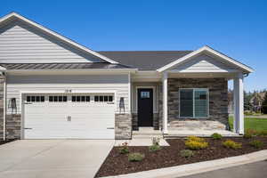 View of front of home with stone siding, concrete driveway, an attached garage, and a standing seam roof