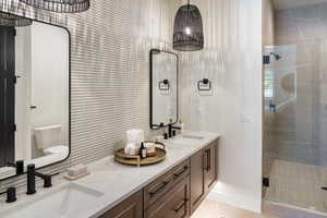 Bathroom featuring double vanity, a stall shower, toilet, and baseboards