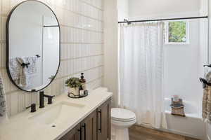 Full bath with vanity, wood finished floors, toilet, shower / bath combo with shower curtain, and tasteful backsplash