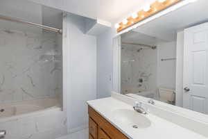 Bathroom with a combined bath / shower with marble appearance, vanity, toilet, marble finish flooring, and baseboards