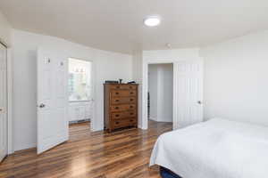 Bedroom with dark wood-style floors, baseboards, and ensuite bath