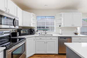 Kitchen with open shelves, appliances with stainless steel finishes, a sink, and healthy amount of natural light