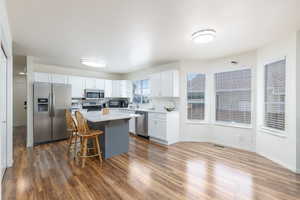 Kitchen featuring appliances with stainless steel finishes, white cabinetry, light countertops, a kitchen island, and a kitchen bar