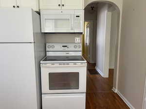 Kitchen with white appliances, arched walkways, dark wood-type flooring, baseboards, and white cabinetry