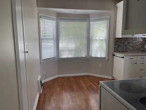 Kitchen featuring electric range oven, white cabinets, wood finished floors, decorative backsplash, and healthy amount of natural light