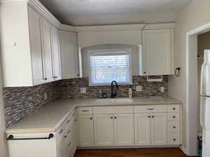 Kitchen with a sink, freestanding refrigerator, white cabinets, and decorative backsplash