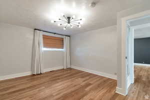 Empty room with a chandelier, light wood-style flooring, baseboards, and a smoke detector