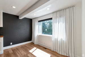 Spare room featuring brick wall, baseboards, light wood finished floors, recessed lighting, and beam ceiling
