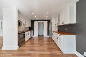 Kitchen featuring stainless steel appliances, a barn door, butcher block counters, light wood-type flooring, and tasteful backsplash