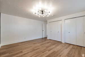 Unfurnished bedroom featuring two closets, light wood-style floors, a chandelier, and baseboards