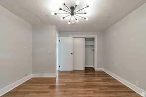 Unfurnished bedroom with a chandelier, a closet, baseboards, and wood finished floors