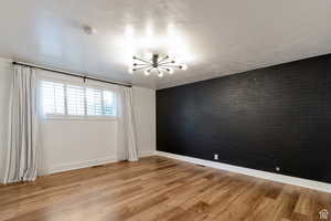 Unfurnished room featuring a chandelier, brick wall, baseboards, a smoke detector, and light wood-style flooring