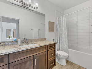 Bathroom featuring wood finished floors, vanity, toilet, and shower / bathtub combination with curtain