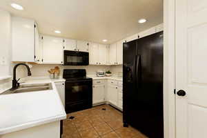 Kitchen with black appliances, a sink, light tile patterned flooring, light countertops, and white cabinets