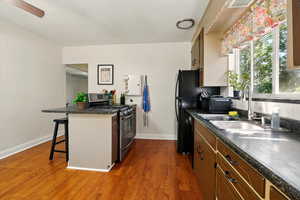 Kitchen with stainless steel gas range, a sink, dark countertops, and a breakfast bar area