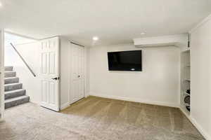 Finished basement with carpet floors, a textured ceiling, baseboards, stairs, and recessed lighting