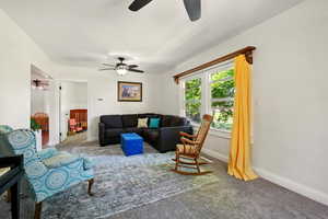 Carpeted living room with a ceiling fan and baseboards