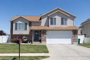Tri-level home featuring brick siding, driveway, an attached garage, and roof with shingles