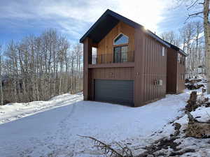 View of snowy exterior featuring a balcony and a garage