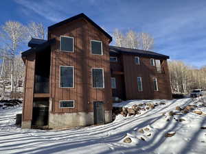 Snow covered property with a balcony, a metal roof, and board and batten siding