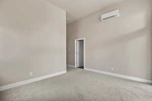 Empty room featuring a wall mounted air conditioner, carpet flooring, and baseboards