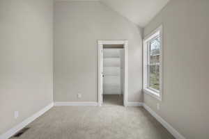 Unfurnished bedroom featuring a walk in closet, carpet floors, lofted ceiling, baseboards, and a closet