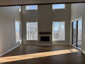 Unfurnished living room featuring a fireplace, a high ceiling, and dark wood finished floors