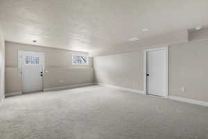 Carpeted spare room featuring a textured ceiling, baseboards, and a smoke detector