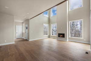 Unfurnished living room with hardwood / wood-style flooring, a glass covered fireplace, a towering ceiling, and baseboards
