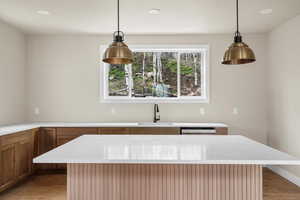 Kitchen with a sink, decorative light fixtures, light stone countertops, recessed lighting, and brown cabinetry