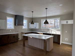 Finished Kitchen with hanging light fixtures, dark wood-style flooring, wall chimney exhaust hood, a center island, and brown cabinetry