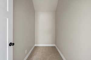 Empty room featuring carpet floors, baseboards, and vaulted ceiling