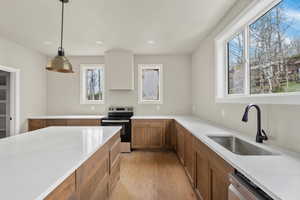 Kitchen with stainless steel appliances, a sink, brown cabinetry, light wood-type flooring, and light stone counters