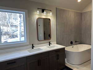 Full bath featuring a soaking tub, double vanity, and lofted ceiling
