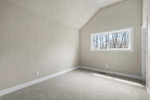 Carpeted spare room featuring lofted ceiling and baseboards