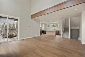 Unfurnished living room featuring light wood-style floors, baseboards, stairway, a sink, and a towering ceiling