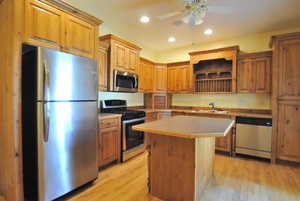 Kitchen with appliances with stainless steel finishes, a sink, light wood-style flooring, a ceiling fan, and a center island