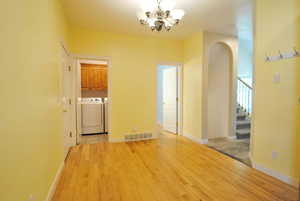 Empty room featuring independent washer and dryer, a chandelier, arched walkways, stairway, and light wood-style flooring
