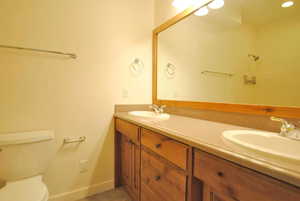 Full bath featuring double vanity, toilet, and baseboards