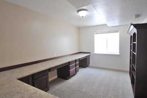 Unfurnished office featuring built in desk, a textured ceiling, light colored carpet, and baseboards