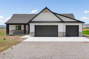 Modern farmhouse with stone siding, an attached garage, and gravel driveway
