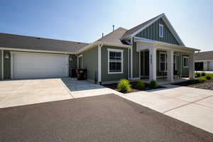 View of front facade featuring a porch, board and batten siding, driveway, a shingled roof, and a garage