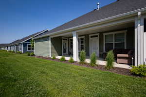 Rear view of house featuring a lawn, a shingled roof, and covered porch