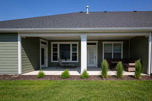 Doorway to property with a shingled roof, covered porch, a yard, and outdoor lounge area