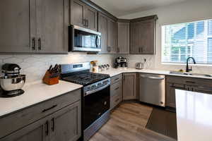 Kitchen with appliances with stainless steel finishes, dark wood finished floors, decorative backsplash, and a sink