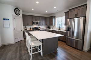 Kitchen featuring appliances with stainless steel finishes, dark brown cabinets, decorative backsplash, a sink, and baseboards